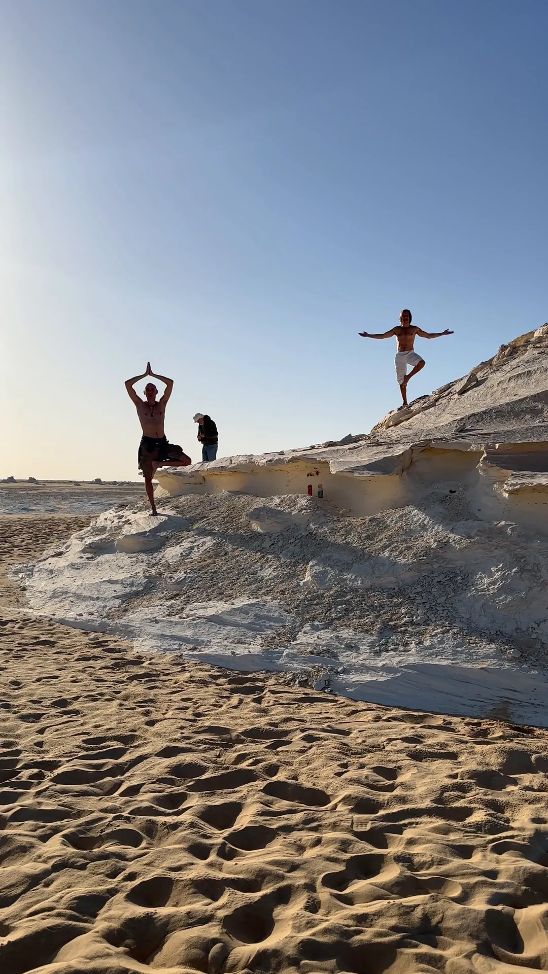 Two people in tree pose on pale sand at sunset
