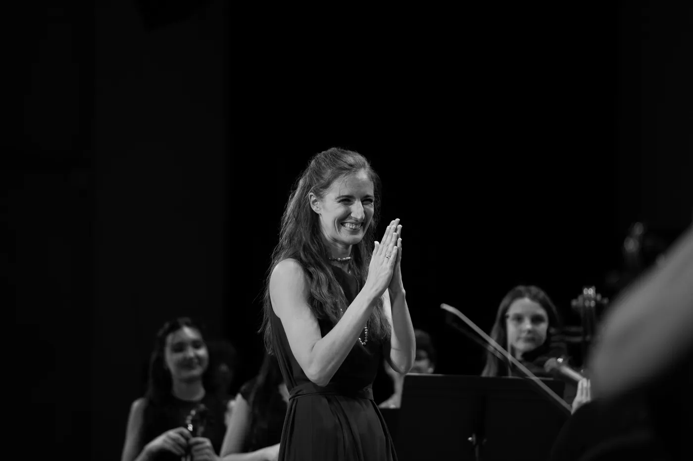 Maria applauding on stage with the orchestra behind her